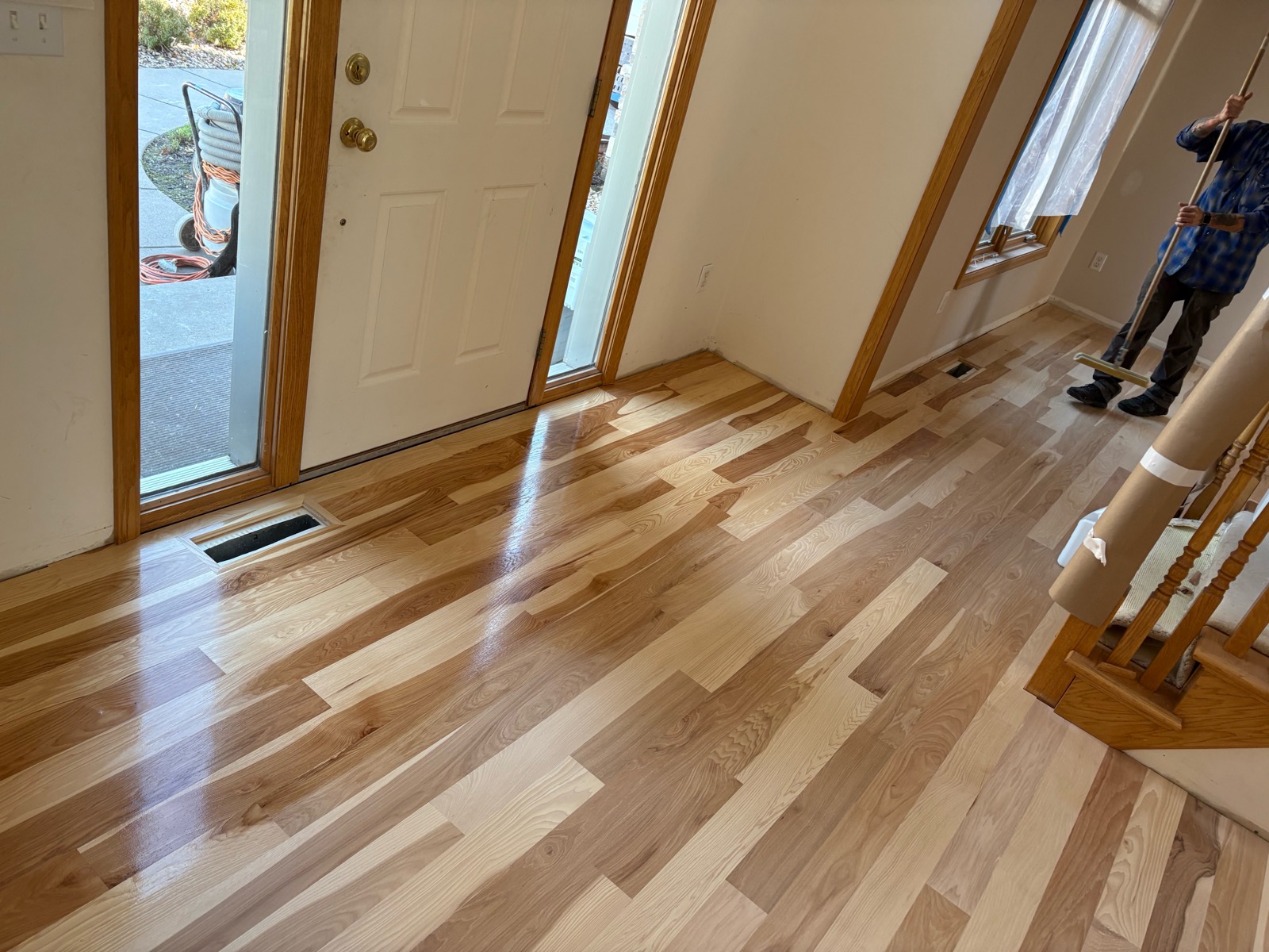Crew member applying a water-based, high-traffic finish to the sanded hickory floor near the entry door and honey oak trim