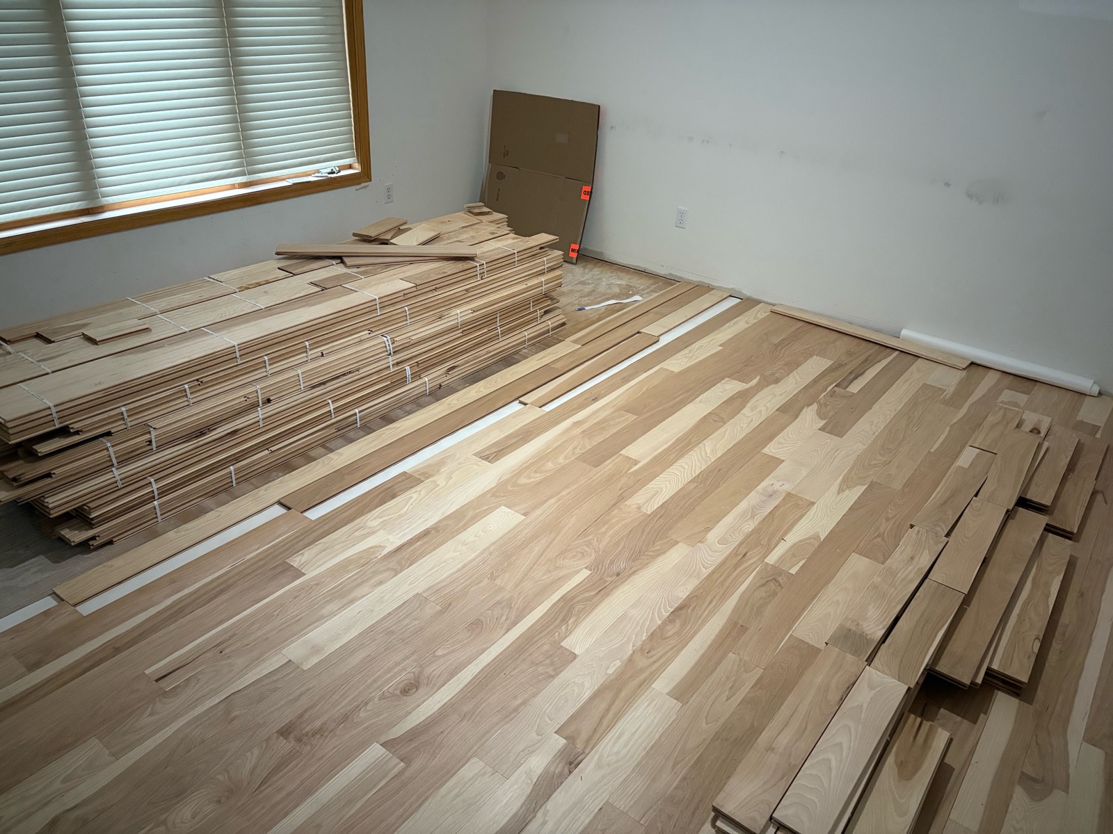 Unfinished solid hickory boards being installed over new subfloor, showing the natural color variation board to board