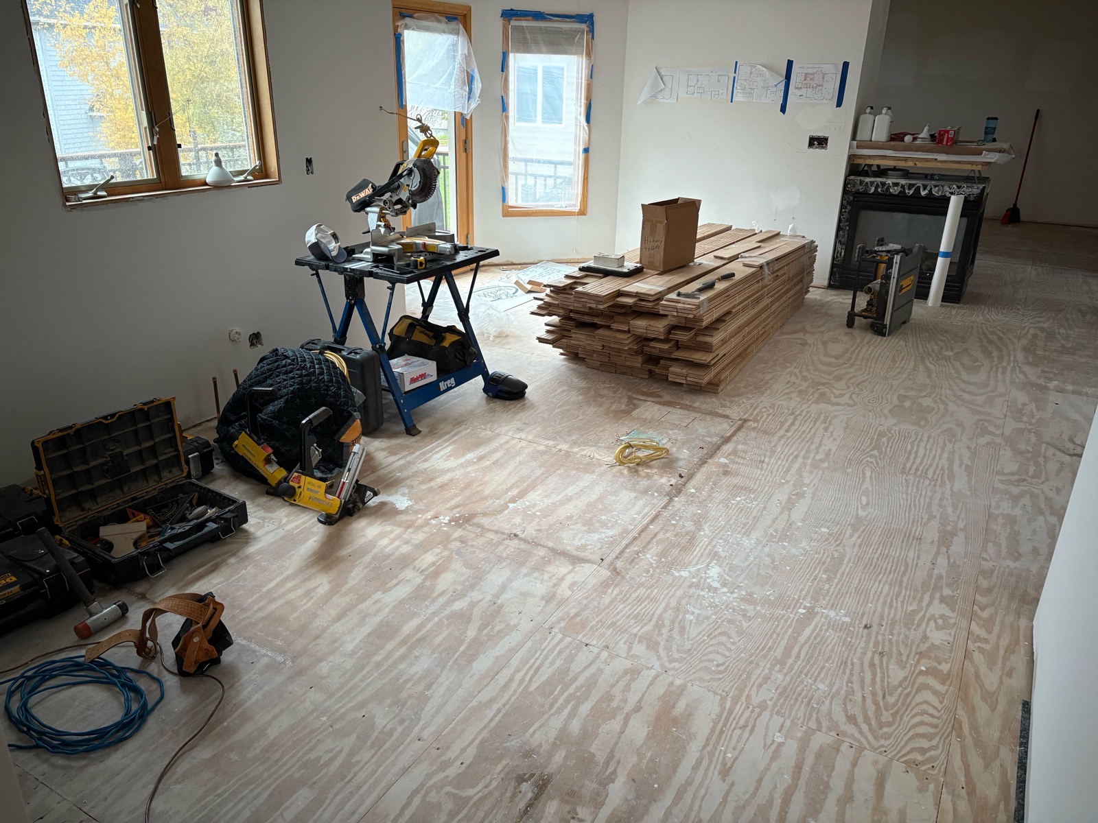 New plywood subfloor installed level across the main level with bundles of hickory flooring staged for install